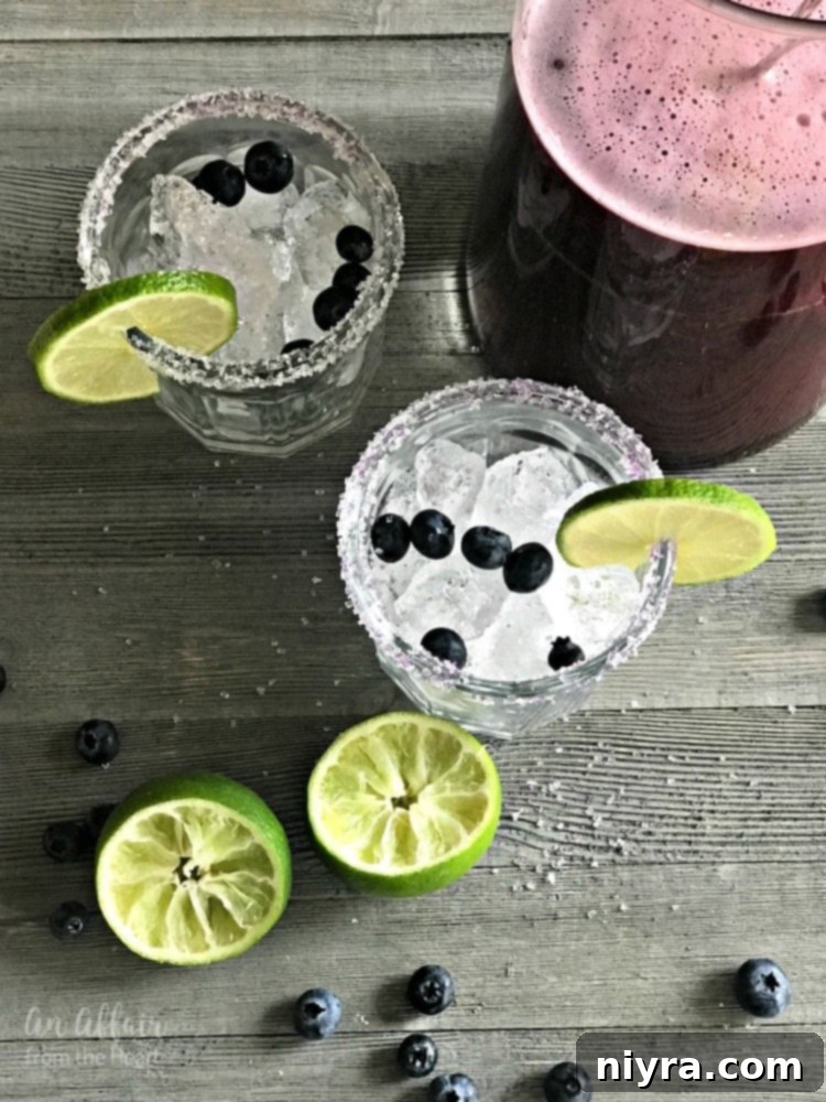 Iced glass of Blueberry Margarita with a pitcher in the background, ready to be served