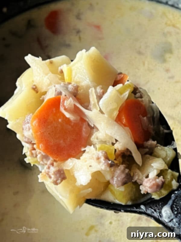 Spoonful of creamy sauerkraut soup with visible vegetables and bratwurst