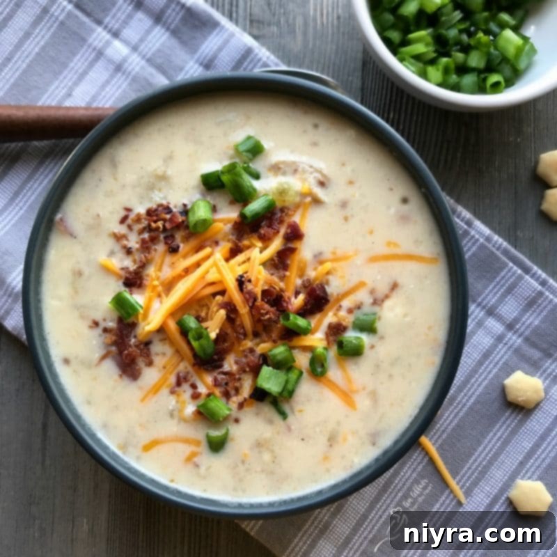 A bowl of creamy Instant Pot Loaded Potato Soup garnished with bacon bits, shredded cheese, and chopped green onions.