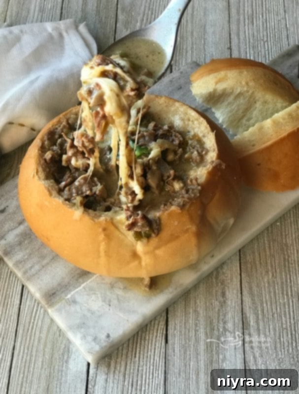 Close-up of Philly Cheese Steak Soup in a bread bowl, showing a delicious cheese pull.