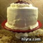 Cherry torte cake on a white cake plate, with decorative piping.