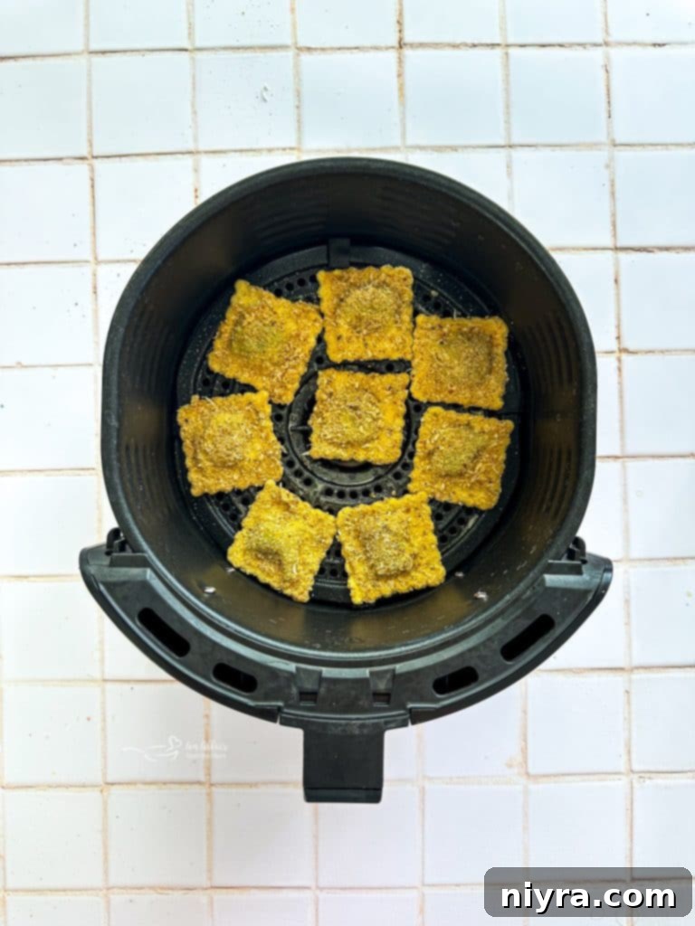 Hand dipping ravioli into breadcrumb mixture after egg wash.