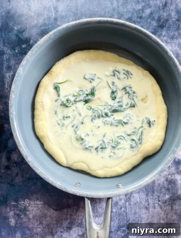 Spreading spinach alfredo mixture over pizza crust, topped with artichokes and mozzarella
