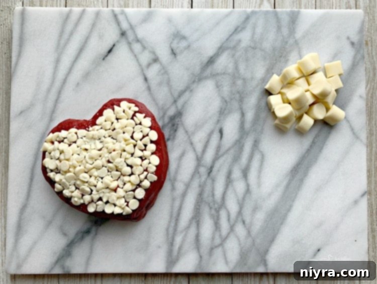 The initial layout of a Valentine's Dessert Cheese Board, featuring a heart-shaped red velvet cheese ball centrally placed, surrounded by various white cheeses, all on a pristine white marble board.