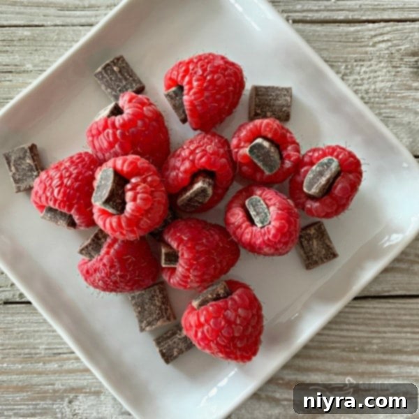 A close-up view of fresh, ripe raspberries, each delicately stuffed with a chunk of dark chocolate, showcasing a delightful and easy gourmet treat for a dessert board.