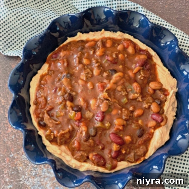 Spreading chili evenly over the refried bean and cheese base in a pie plate