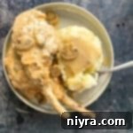 Mantar Soslu Domuz Pirzolası 15 Pork chops with mushroom gravy, a fork and mashed potatoes on a cream color plate.