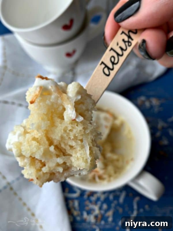 A spoonful of moist Coconut Mug Cake with whipped cream and toasted coconut