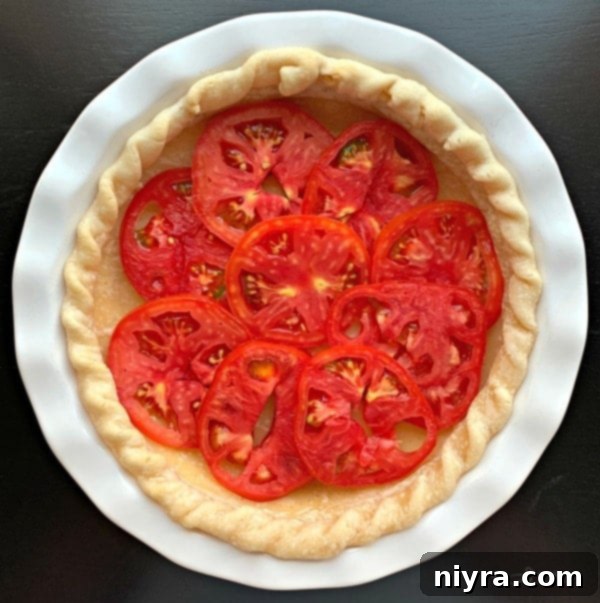 First layer of sliced tomatoes placed in a pre-baked pie crust