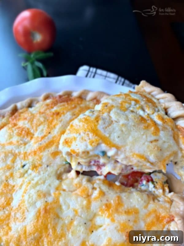 A generous slice of Southern Tomato Pie showing layers of tomatoes, cheese, and herbs