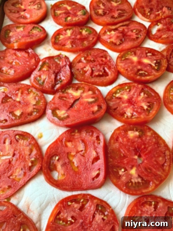 Sliced red tomatoes laid out on paper towels for draining