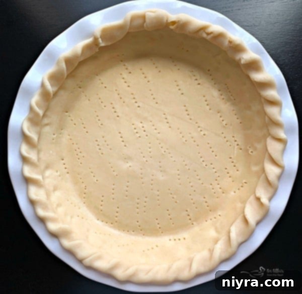 Unbaked pie crust in a pie plate, poked with fork tines