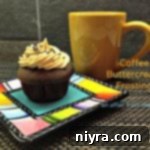 Decadent Coffee Buttercream 2 Side view of a cupcake plated next to a cup of coffee, both adorned with coffee buttercream frosting.