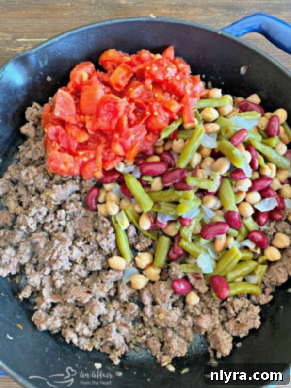 Adding drained Paisley Farm Five Bean Salad and diced tomatoes to ground beef