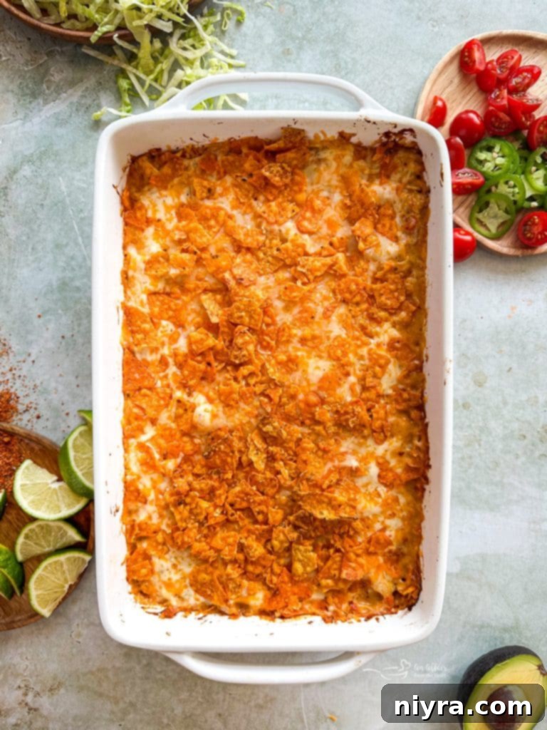 Assembled casserole layers with Doritos, chicken mixture, and cheese.