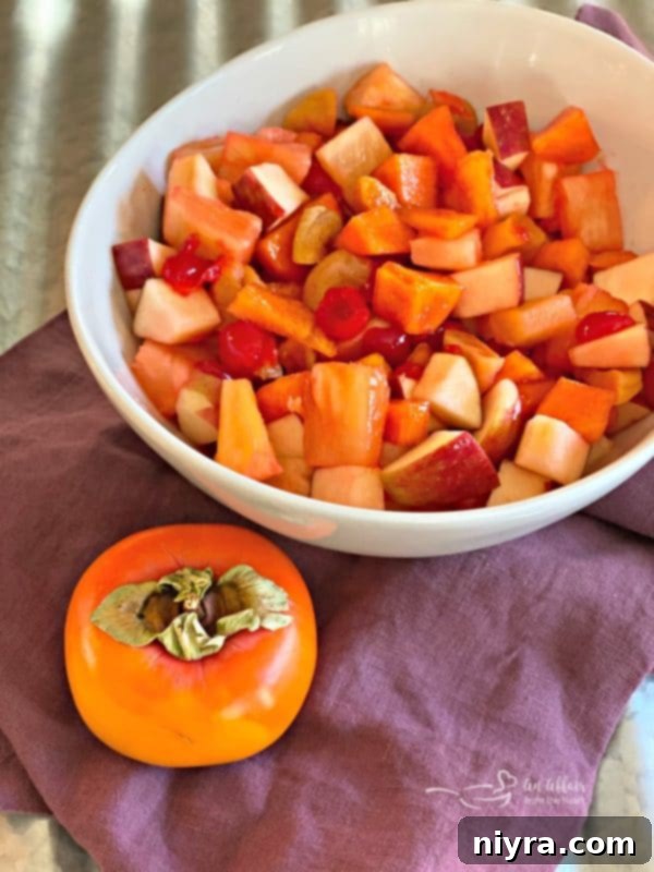 A vibrant Persimmon Salad in a white bowl, featuring chunks of persimmon, apple, maraschino cherries, pineapple, and apricots.