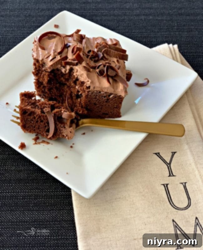 A generous swirl of rich, fluffy Chocolate Pudding Frosting on a piece of cake, with a spoonful removed revealing its creamy texture.