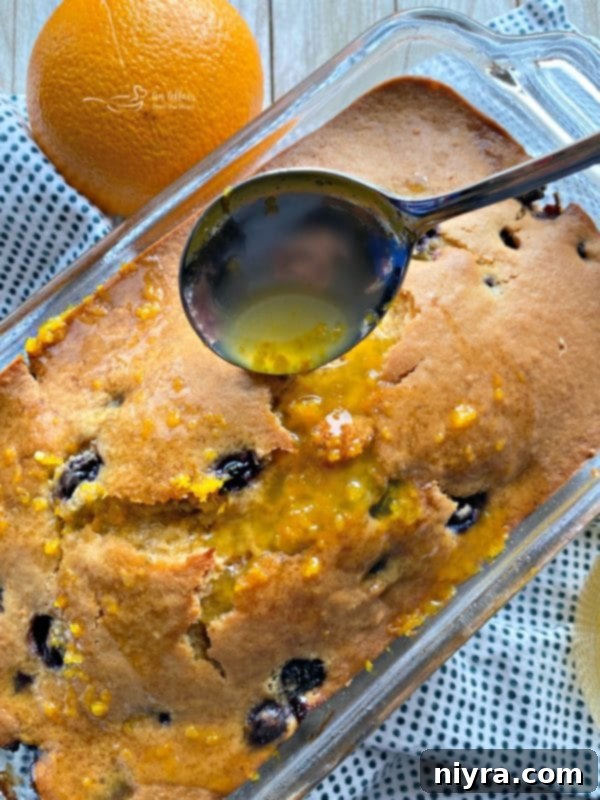 Zesty Orange Blueberry Loaf 9 Blueberry Orange Bread with a glistening honey-orange glaze being poured over it.