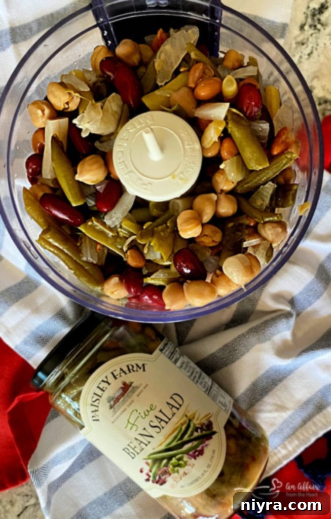 Close-up of a jar of Paisley Farm Five Bean Salad being drained in a colander in a sink, showing the colorful mix of beans.