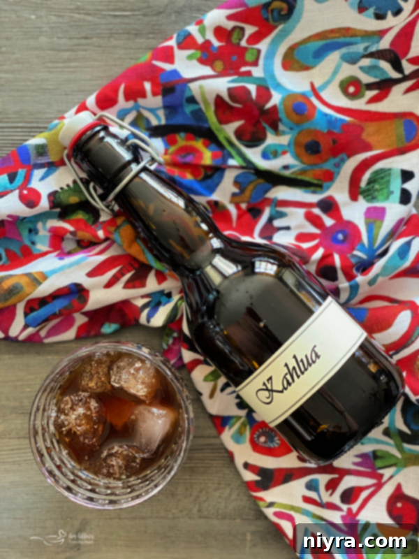 A bottle of homemade Kahlua liqueur next to a glass filled with the dark amber liquid, garnished with coffee beans.