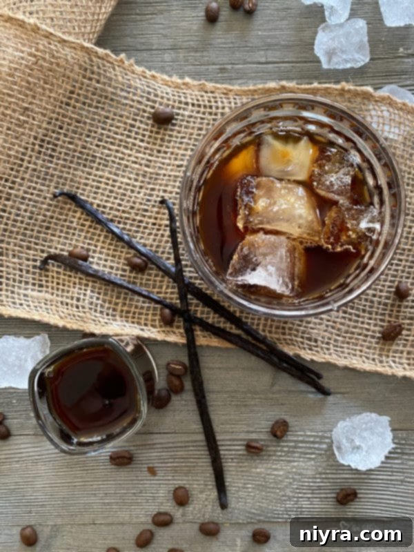 A bottle of homemade Kahlua being poured into a glass with ice and coffee beans.