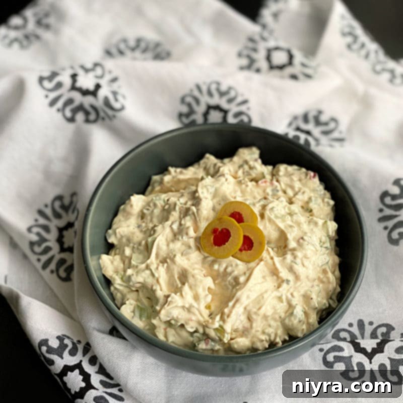 Creamy olive dip in a bowl, garnished with sliced olives and served with crunchy crackers.
