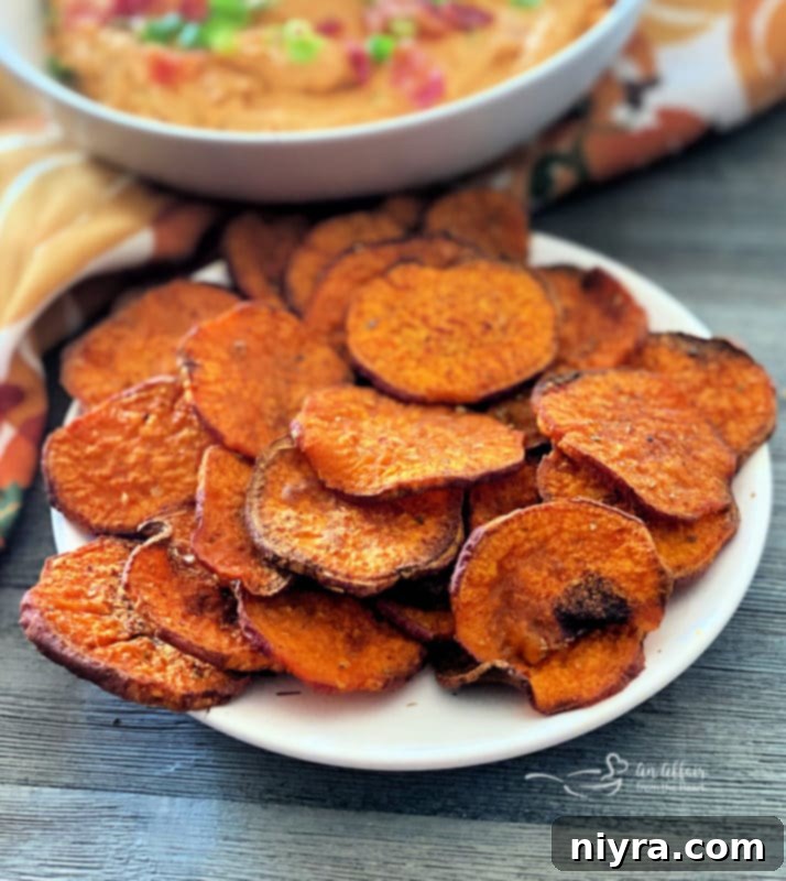 A bowl of freshly baked sweet potato chips, perfectly golden and crispy, garnished with a sprinkle of fresh herbs.