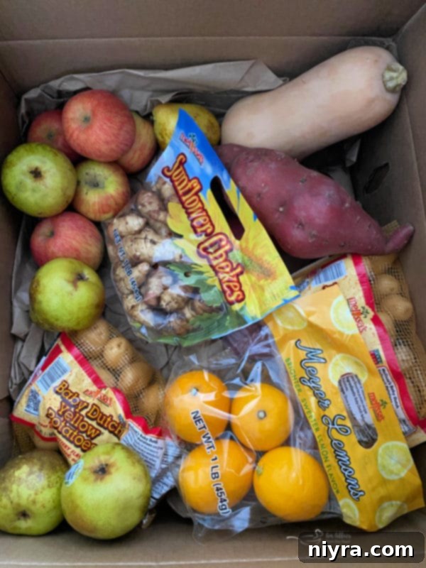A vibrant box of fresh produce from Melissa's, featuring pears, butternut squash, apples, lemons, baby potatoes, sunflower chokes, and yams.