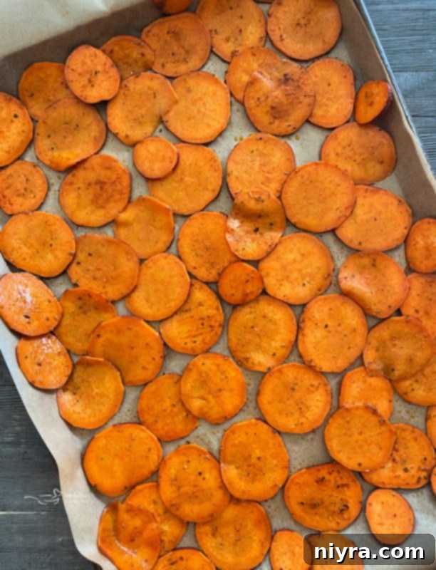 Thinly sliced and seasoned sweet potato chips spread in a single layer on a parchment-lined baking sheet.