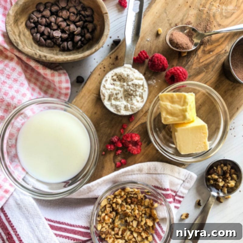 Ingredients for a mug brownie laid out on a white surface, including butter, milk, hot cocoa mix, flour, and chocolate chips.