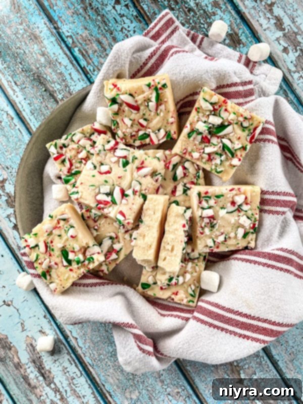A small stack of White Chocolate Peppermint Fudge squares on a cooling rack, with crushed candy canes scattered around.