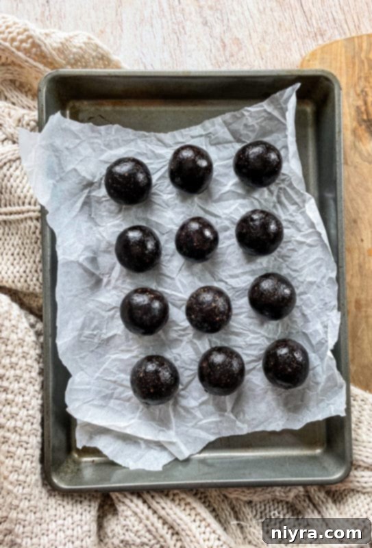 Decadent Bittersweet Chocolate Bourbon Balls 7 Hands rolling the chocolate and bourbon mixture into small, perfectly round balls on a parchment-lined baking sheet.