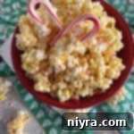 Close up of Peppermint Candy coated popcorn and 2 candy canes in a red bowl