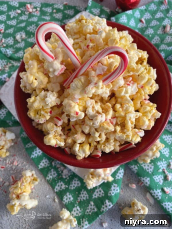 A large white bowl filled with peppermint candy-coated popcorn with crushed candy canes.
