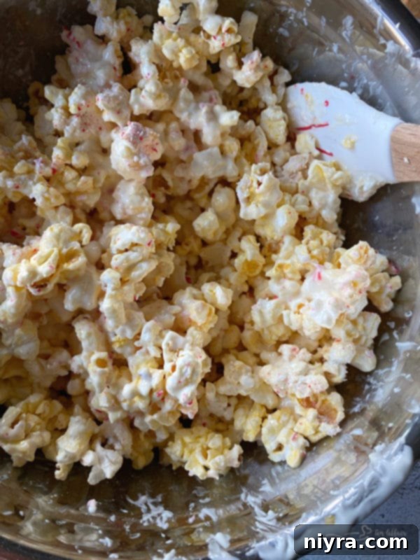 Melted almond bark being poured over popped popcorn in a large bowl.