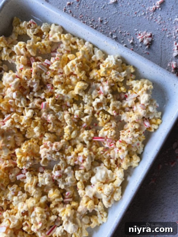Peppermint bark popcorn being mixed in a bowl with crushed candy canes.