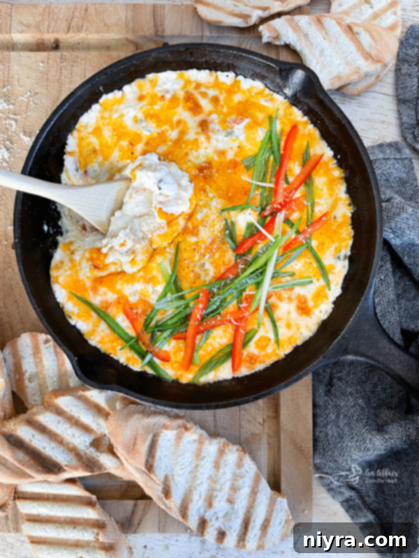 Slow Cooker Crab Dip served in a bowl, garnished with green onions and red peppers, with crackers on the side.