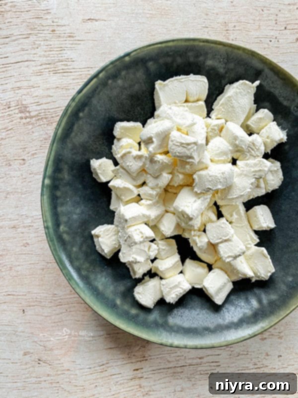 A close-up of ingredients for Slow Cooker Crab Dip being added to the slow cooker, showing cubed cream cheese and crabmeat.