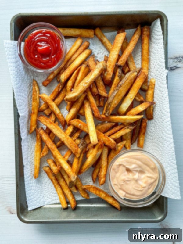 Perfectly Crispy Homemade French Fries 13 Homemade double fried french fries on baking sheet with parchment paper, ketchup, and sauce, displaying a full spread of crispy goodness
