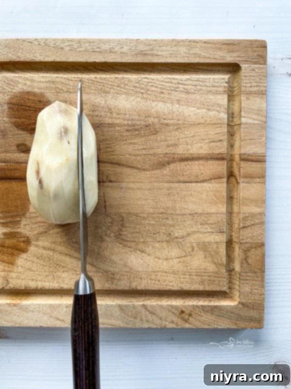 Perfectly Crispy Homemade French Fries 7 One peeled potato being sliced on wooden cutting board, demonstrating the initial preparation step