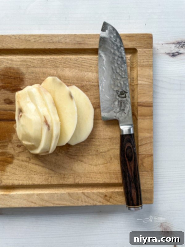 Perfectly Crispy Homemade French Fries 8 Top view of peeled sliced potato on wooden cutting board with knife, illustrating the precise cutting process