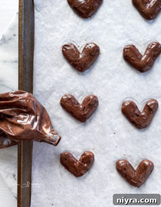 Piping chocolate cake batter onto parchment paper in heart shapes for whoopie pies