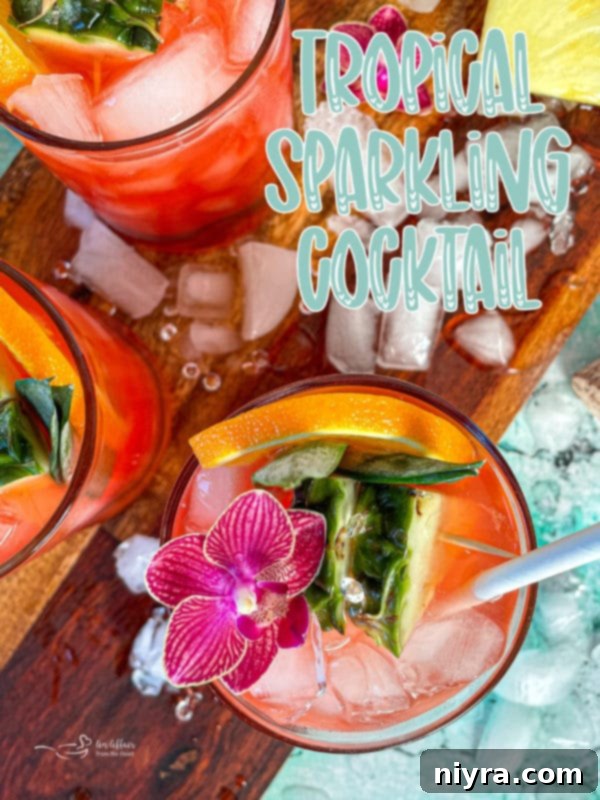 A hand holding a garnished Tropical Sparkling Cocktail against a bright, airy background