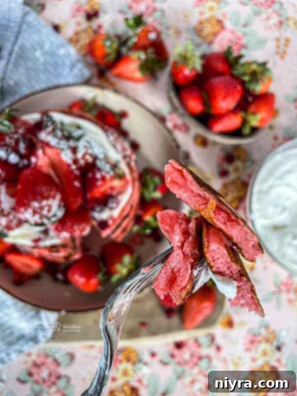 Dreamy Strawberry Pancakes 12 A close-up of a stack of strawberry pancakes with a subtle pink tint, adorned with fresh strawberry slices and a light dusting of powdered sugar, ready to be served.
