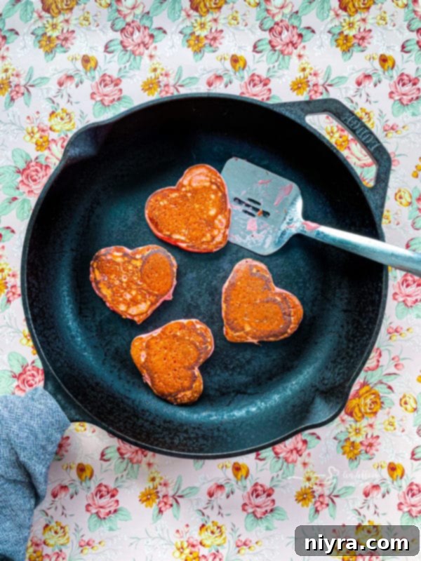 Dreamy Strawberry Pancakes 9 Heart-shaped strawberry pancakes cooking on a griddle, showing the perfect golden-brown color and fluffy texture.