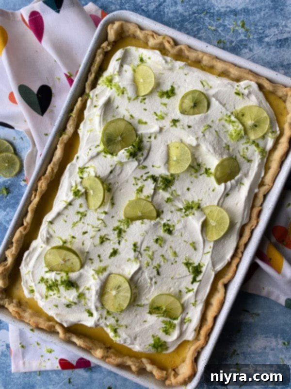 A vibrant Key Lime Slab Pie, topped with freshly whipped cream and lime slices, ready to be served.