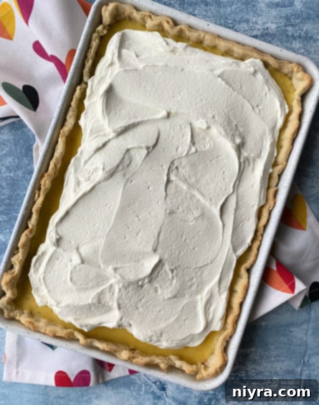 A pastry bag piping whipped cream onto the cooled Key Lime Slab Pie.