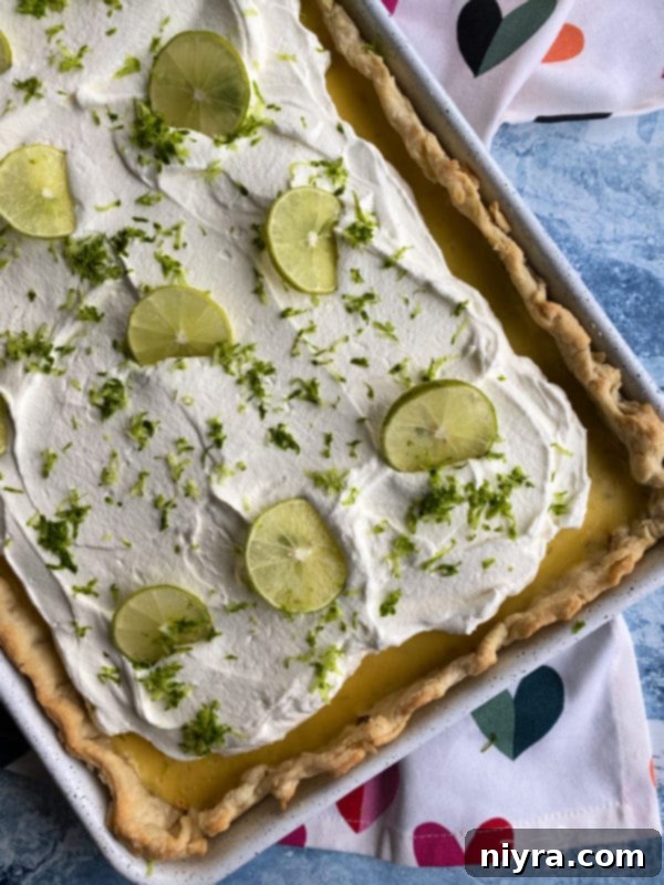 Finished Key Lime Slab Pie, topped with whipped cream and garnished with fresh lime slices and zest.