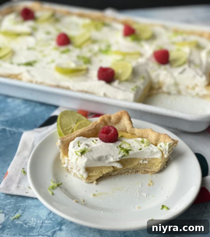 A close-up shot of Key Lime Slab Pie, showcasing the smooth, pale yellow custard and fluffy white whipped cream topping, garnished with fresh raspberries.