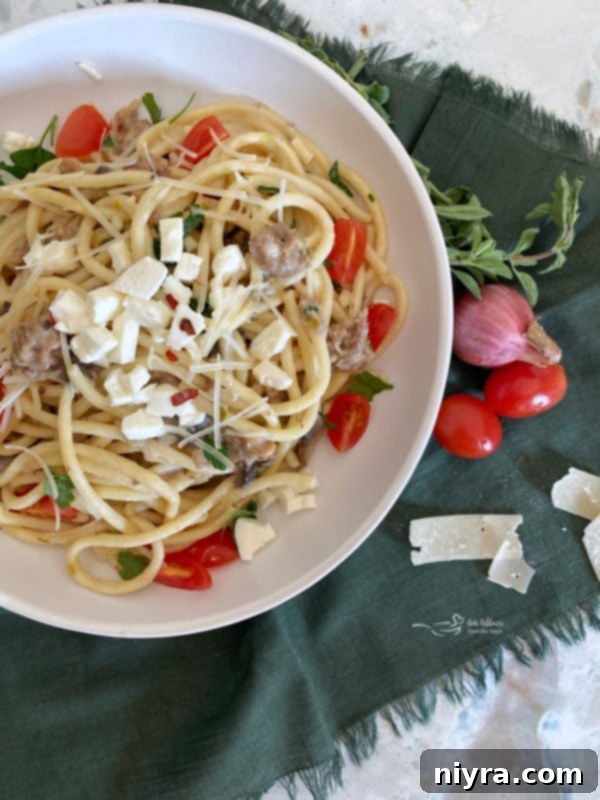 Top view of bucatini in a white bowl with tomatoes and mozzarella